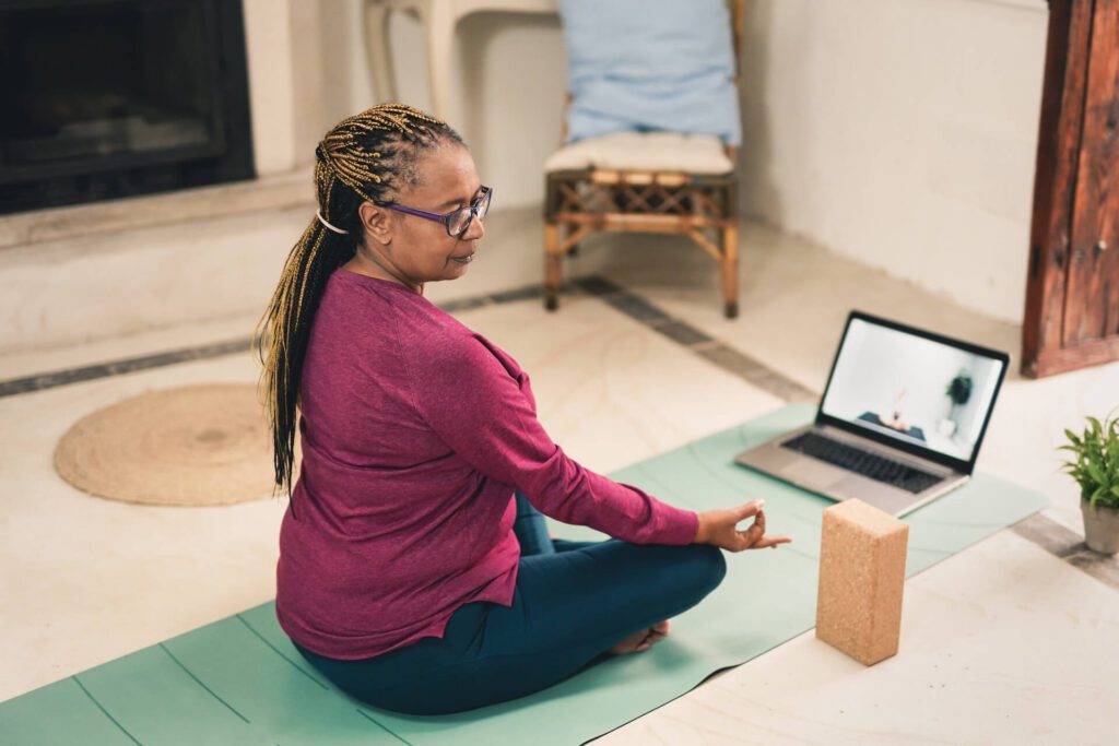 A woman sits in a yoga pose during a virtual yoga session at home