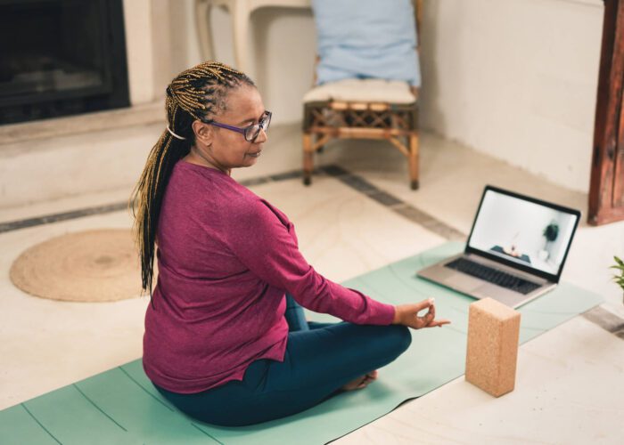 A woman sits in a yoga pose during a virtual yoga session at home