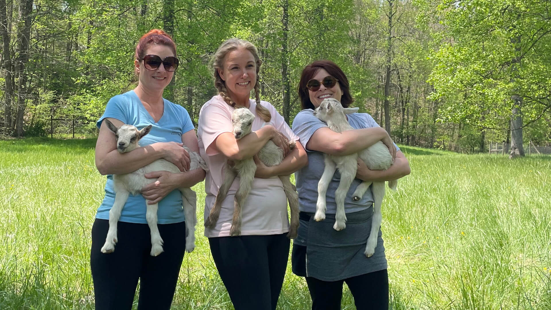 Three women holding baby goats.