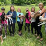 Women's group in Asheville, NC holding baby goats in a field after a goat yoga session.