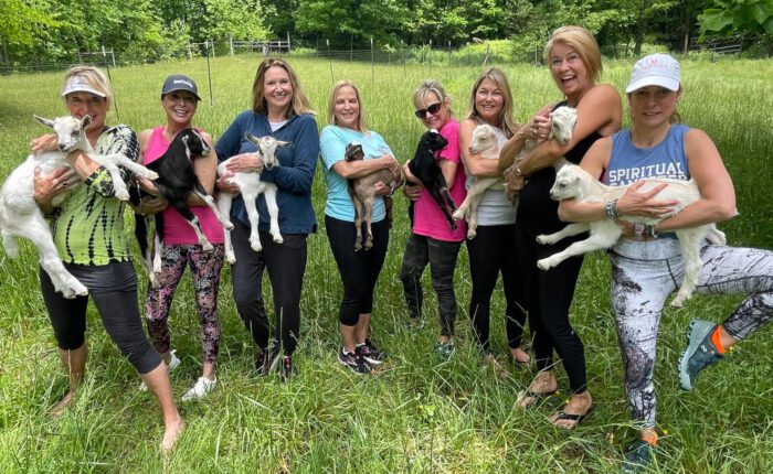 Women's group in Asheville, NC holding baby goats in a field after a goat yoga session.