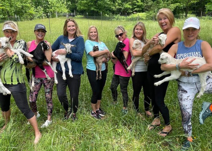 Women's group in Asheville, NC holding baby goats in a field after a goat yoga session.