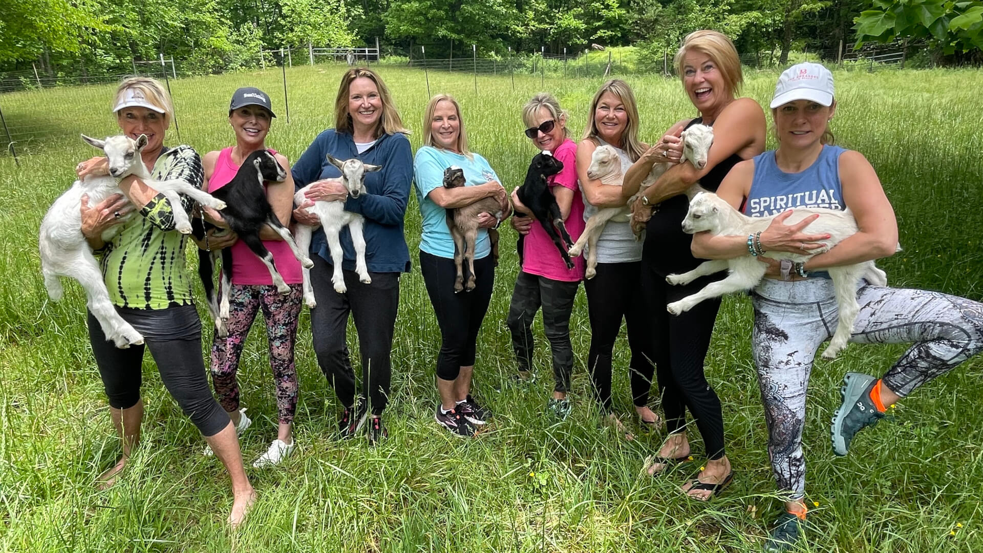Women's group in Asheville, NC holding baby goats in a field after a goat yoga session.