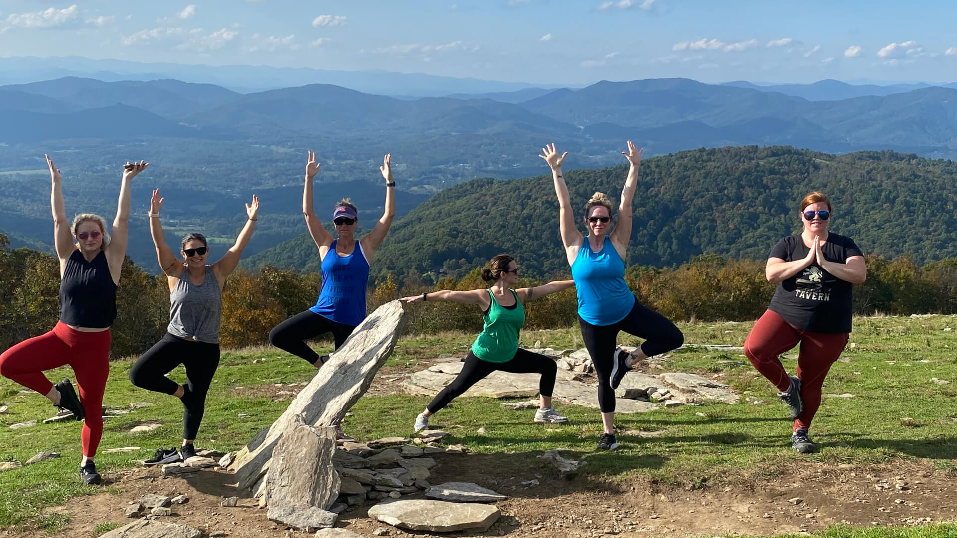 Women in various yoga poses on yoga hike on mountaintop in Asheville, NC.