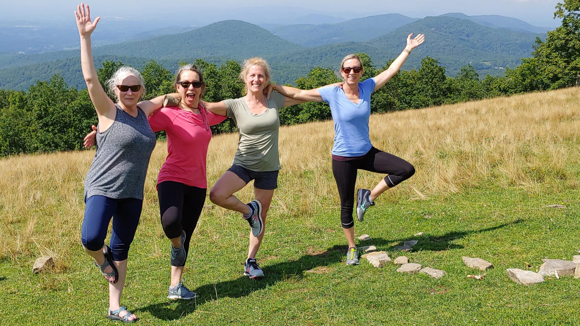 Summer mountaintop yoga hike in Asheville, NC featuring four women in tree pose